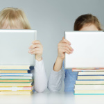 Two pupils leaning on a pile of books while reading on touchpad